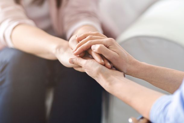Two women hold hands comfortingly.