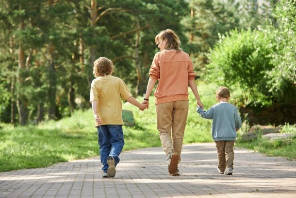Back view of mother holding hands with two boys as they walk on a trail.