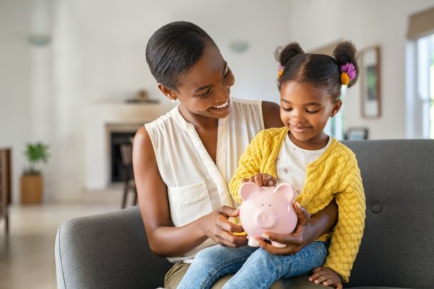 A woman with her child on her knee holding a piggy bank.