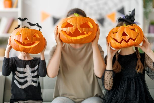 A mother and two children holding up carved pumpkins to their faces.