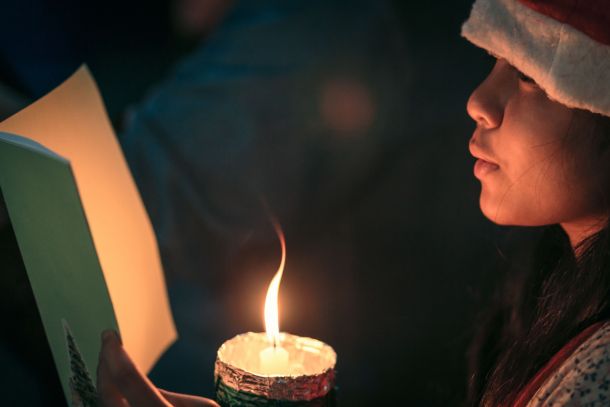 A child singing a Christmas carol by candlelight.