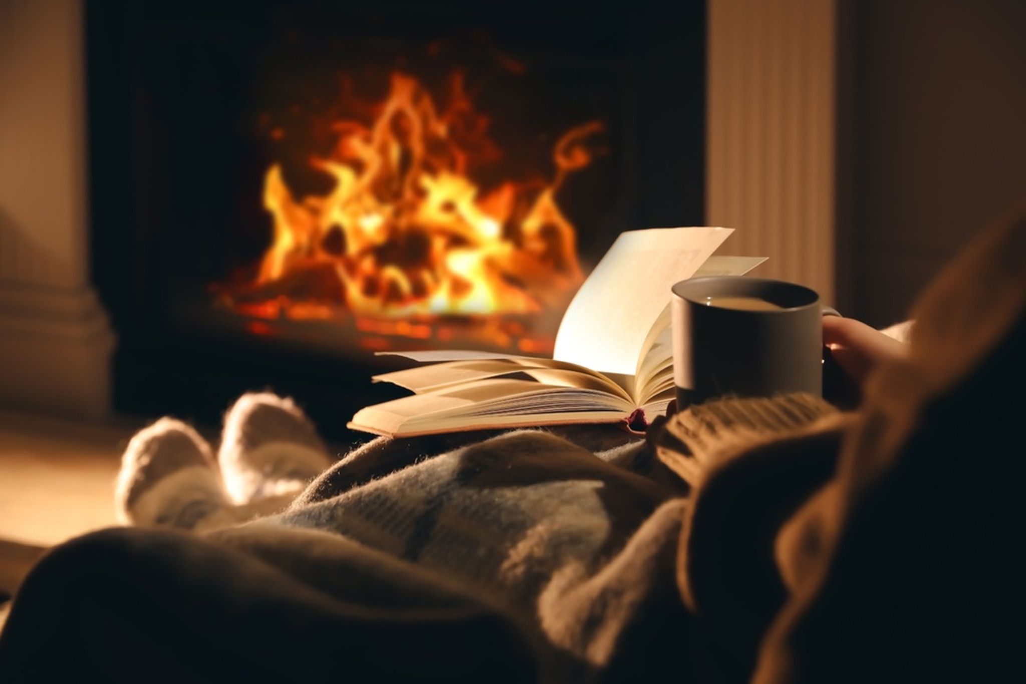 Person sitting with their feet up reading by an open fire