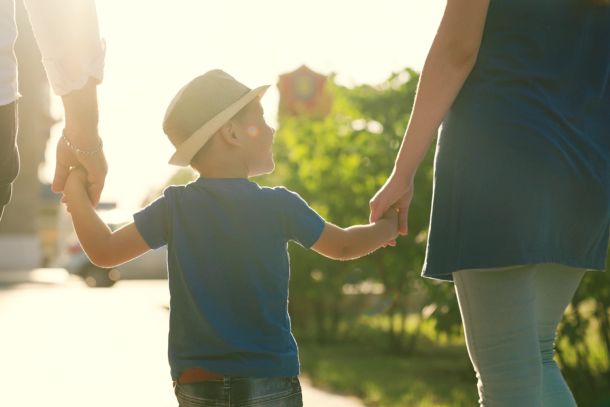 A family with a young child holding hands outdoors.