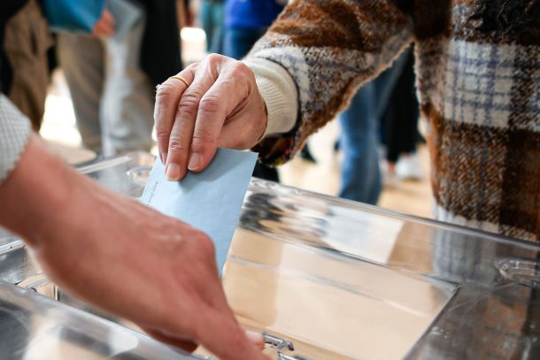 A person putting a ballot paper into a box.