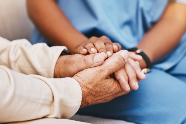 An elderly person holding hands with a nurse.